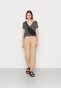 Top preto de flores com mangas curtas e decote em V, calças largas bege e sandálias pretas com detalhe de fivela. Acessório: mala de ombro preta.