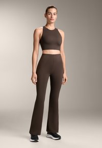 Barna sportos crop top és harang szabású leggings sima anyagból, zökkenőmentes dizájnnal, fekete sportcipővel viselve.