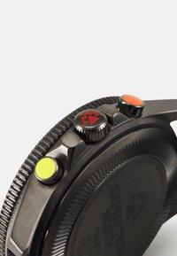 Montre pour homme avec un boîtier métallique noir, comportant trois boutons-poussoirs : un jaune, un orange et une couronne avec des accents rouges. Lunette striée texturée.