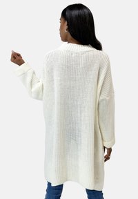 Cardigan lungo e oversize di colore crema realizzato in tessuto a maglia, con colletto e maniche a coste, dalla silhouette morbida e design con schiena aperta.
