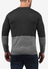 Pull en tricot gris et gris foncé avec un col rond côtelé et des manches longues. Présente une texture lisse et un design en blocs de couleur.