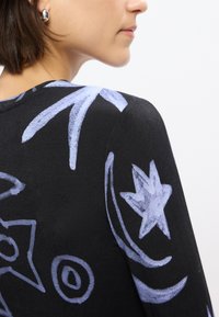 Μαύρο ένδυμα με αφηρημένα σχέδια  σε ανοιχτό μπλε, περιλαμβάνοντας αστέρια και σπείρες. Λείο υλικό; κοντινός φακός στην περιοχή του ώμου.