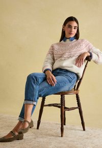 Wollpullover in Creme mit pinkem geometrischem Muster, blaue Jeanshemd und hochgekrempelte Jeans. Olivgrüne, niedrigabsatzige Schuhe mit Schnallen-Detail.