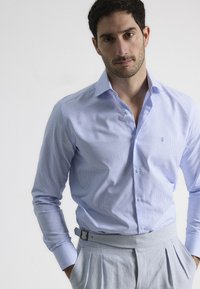 Camisa de vestir de cuadros azul claro con mangas largas y cuello abotonado, combinada con pantalones de tela gris claro con pinzas y un cinturón.