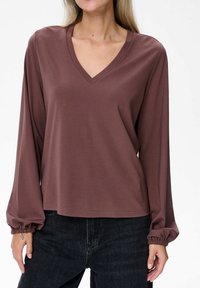 Bruine lange mouwen v-hals top gemaakt van een soepele stof, metGathered cuffs en een relaxte pasvorm, gecombineerd met zwarte broek.