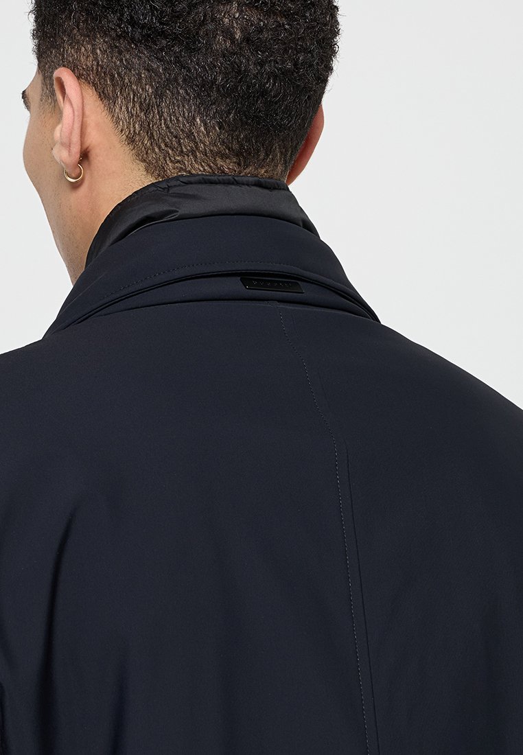 Dunkelblau Herrenjacke mit hohem Kragen, glatter Textur und dezenten Nähten. Verfügt über ein markantes Logo im Nackenbereich.