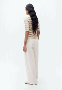 Gestreepte geribbelde trui in beige en crème, gecombineerd met ruime crème broek. Vloeibare textuur, casual pasvorm, geen zichtbare patronen of accenten.