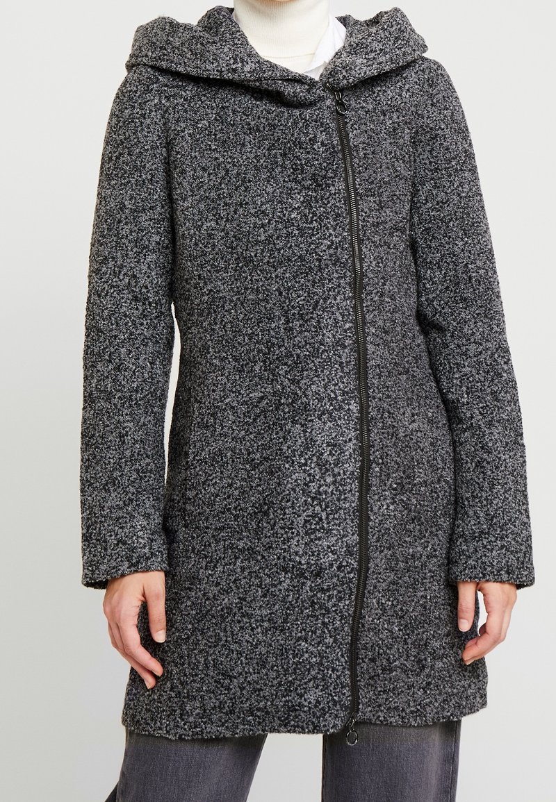 Manteau gris texturé avec fermeture éclair, capuche et manches longues. Le tissu présente un motif moucheté, offrant chaleur et douceur.