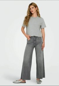 Camiseta gris combinada con jeans de mezclilla gris de pierna ancha y cintura alta. Modelo lleva zapatos metálicos tipo slip-on. Diseño sencillo con un ajuste relajado.