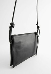 Čierna kožená crossbody taška s textúrovaným povrchom, so zipsovým uzáverom a uzlovým detailom na popruhu, ktorá sa vyznačuje jednoduchým obdĺžnikovým dizajnom.