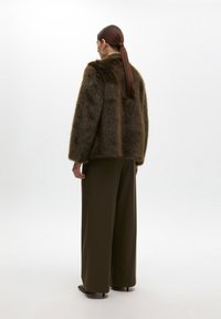 Brown faux fur coat with a relaxed fit, featuring a high collar and slightly oversized sleeves, paired with wide-leg dark green trousers.