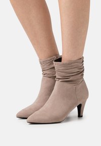 Botas de tobillo de ante beige con un diseño arrugado, punta afilada y un tacón de 6.5 cm. Textura suave y silueta simple.