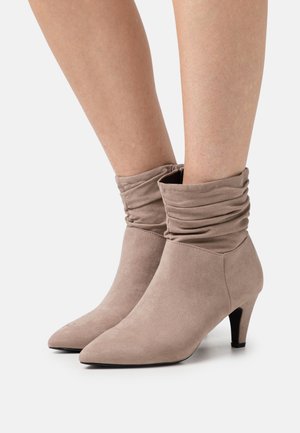 Bottines en suède beige avec un design plié, bout pointu et un talon de 6,5 cm. Texture lisse et silhouette simple.
