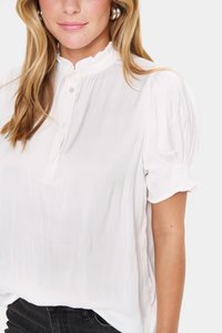 Blusa bianca leggera con colletto arricciato alto e maniche a sbuffo corte. Presenta una chiusura a bottoni sul davanti e una texture liscia.