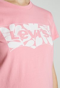Růžové bavlněné tričko s bílým logem Levi's a květinovým grafickým designem, s klasickým kulatým výstřihem a krátkými rukávy.