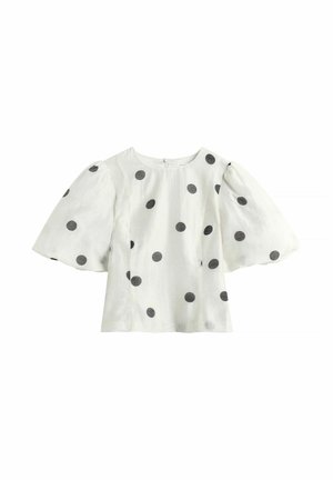 Witte blouse met grote zwarte polkadots en brede, opgeblazen korte mouwen, met een ronde halslijn en een ritssluiting aan de achterkant.