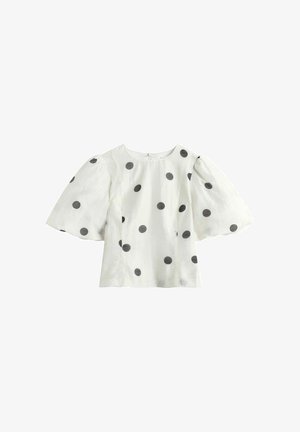 Hvid bluse med store sorte polkaprikker og brede, pufærmer i kort længde, med rund halsudskæring og lynlås bagpå.