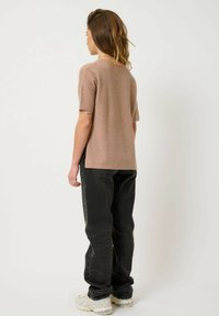 Lys brun kortærmet sweater lavet af blødt materiale, parret med mørke jeans. Tøjet har en afslappet pasform og enkle, rene linjer.