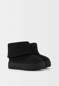 Bottes noires à la cheville avec un dessus en tricot côtelé, en daim doux, doté d'une épaisse semelle plateforme texturée pour plus de hauteur.