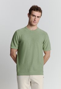 Lichtgroene sweater met korte mouwen en een ronde hals, gemaakt van een zacht, gestructureerd materiaal. Bevat een geribbelde onderrand en manchetten.