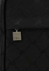 Borsa nera in tessuto con motivo in rilievo, dotata di un'etichetta metallica con il logo Fila. Chiusura con zip e texture liscia. Design compatto con forma strutturata.