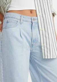 Jeans in denim azzurro chiaro con una vestibilità comoda, caratterizzati da tasche frontali, chiusura con bottone e leggere sfumature. Abbinati a una camicia a righe.