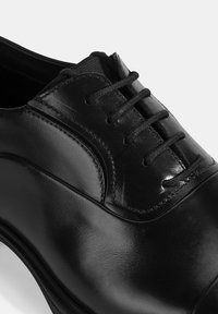 Zwarte leren dress shoe met een gladde afwerking, ronde neus en zes oogjes voor de vetersluiting met zwarte veters. Subtiele stiksels.