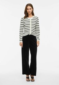 Svart- och vitrandig cardigan med rund halsringning, knappstängning och figurnära ärmar, i kombination med svarta vida byxor och svarta sandaler.