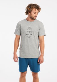 Grijze katoenen t-shirt met een centraal profiel waarop "POV" en "PROTEST SPORTSWEAR EST.93" staat. Gecombineerd met blauwe shorts staat het model in een neutrale houding.