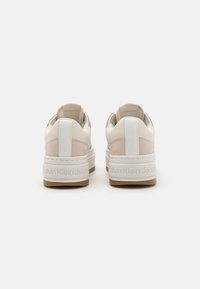 Hvite og lyserosa sneakers med teksturert overflate, som har tykk såle, preget merkenavn og glatte skinnakenter på hælen.