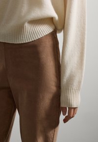 Cream ribbed sweater with wide cuffs paired with brown corduroy pants. The sweater features a relaxed fit, while the pants have side zippers.