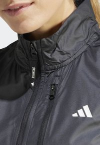 Czarna kurtka do biegania z wysokim kołnierzem, wyposażona w zamek błyskawiczny z przodu i detal z logo. Gładka tekstura i lekka konstrukcja.