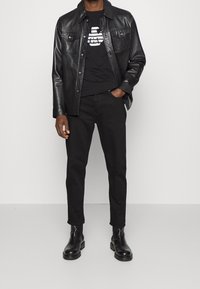 Svart läderjacka över en svart t-shirt med tryck, kombinerat med svarta byxor och stövletter, för en monokrom look.