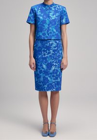 Modrý květinový dvoudílný outfit se skládá z krátkého rukávu crop saka a přiléhavé tužkové sukně, obě z texturované látky s detaily knoflíků.