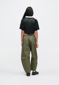 Svart kort ärmtröja för sport med texturerad rygg, kombinerad med lösa olivgröna byxor med elastisk midja och svarta skor.