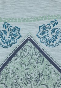 Textil con un fondo azul claro adornado con paisleys en azul marino y verde, junto a patrones decorativos en los bordes. Incluye una etiqueta con texto.