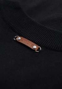 Pull en maille noir avec un col côtelé et une étiquette en cuir marron avec des éléments en métal argenté. L'étiquette arbore le nom de la marque en lettres en relief.