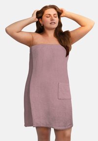 Rosa Handtuchumhang aus strukturiertem Baumwollmaterial, mit einem trägerlosen Design und einer Fronttasche mit eingeprägtem Branding. Weich und saugfähig.