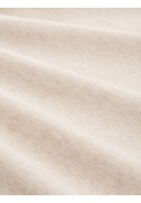 Tissu beige clair avec une texture douce et lisse, présentant des motifs subtils et des nuances variées créées par les fibres tissées.