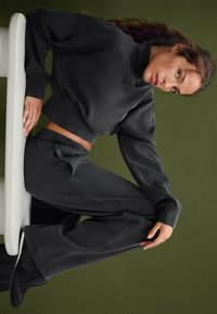 Felpa nera corta con collo alto e taglio morbido, abbinata a pantaloni tapered coordinati. Tessuto morbido con cuciture minime e vita elasticizzata.