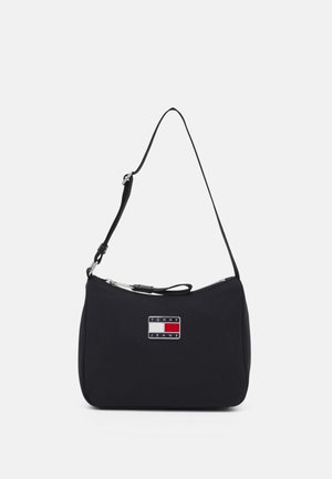 Schwarze Nylon-Schultertasche mit einem silbernen Reißverschluss, ausgestattet mit einem Logo-Plakette mit roten, weißen und blauen Akzenten. Kompakte, geschwungene Form.