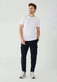 White cotton t-shirt paired with navy cargo pants, featuring side pockets and a straight fit. Worn with silver athletic shoes.