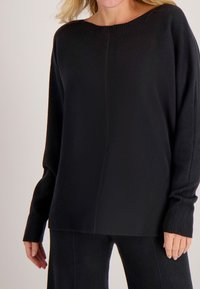 Zwarte gebreide trui met brede halslijn, lange mouwen, geribbelde manchetten en een comfortabele pasvorm. Zachte textuur, minimalistisch ontwerp en effen kleur.