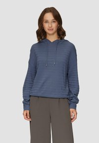 Blauwe hoodie met gestructureerde strepen, lange mouwen en verstelbare koorden. Gecombineerd met losse grijze broeken.