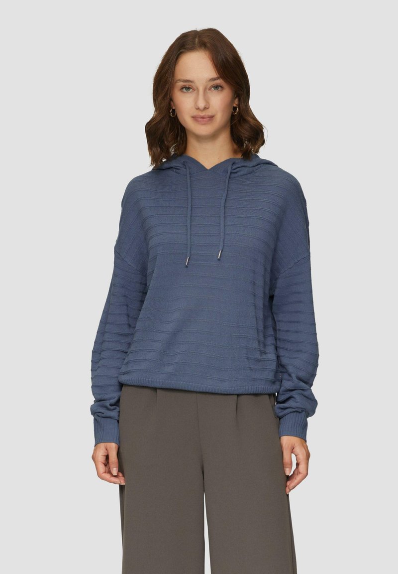 Blauwe hoodie met gestructureerde strepen, lange mouwen en verstelbare koorden. Gecombineerd met losse grijze broeken.