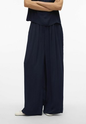 Pantalones de pierna ancha en color navy con pliegues, fabricados en un material ligero y con un ajuste relajado. Combinados con una blusa a juego, creando un look cohesivo.
