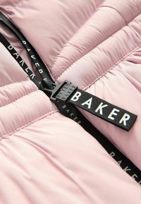 Pamatota rozā jaka ar melnu rāvējslēdzēju, izteikta zīmola etiķete ar "BAKER" un quiltēta tekstūra izolācijai.