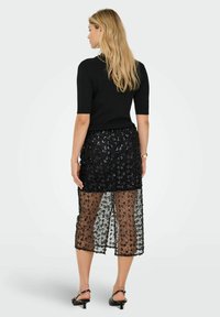 Melns īsroku krekls kombinācijā ar caurspīdīgu melnu svārku ar ziedu rakstiem un spīdumiem, kas beidzas puslīdz kājām, ar atvērtām sānu šķirbām.