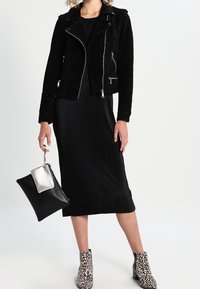 Schwarze Wildleder-Bikerjacke mit silbernem Zubehör, schwarzes geripptes Kleid, schwarze und silberne Clutch sowie Ankle Boots mit Leopardenmuster.