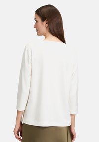 Weißes Langarmshirt mit rundem Ausschnitt, glatter Textur und lockerem Schnitt. Nahtdetails sind an Ärmeln und Saum sichtbar.